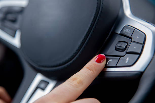 the finger of a female hand push the phone calling button on the steering wheel, the equipment of a modern car. close-up, soft focus, blur background stock photo