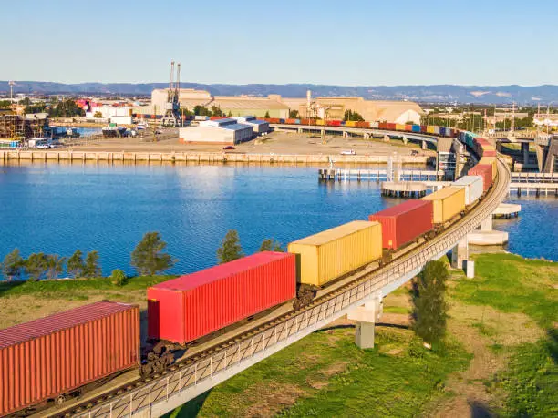 Photo of Colourful freight train with shipping containers crossing river railway bridge with waterfront docks