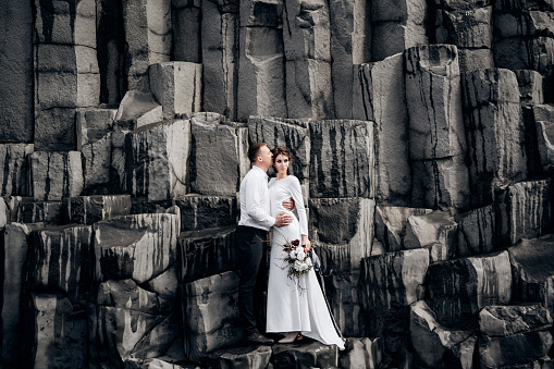 Una pareja de bodas se para en una pared de pilares de piedra. Los novios se abrazan en kekurs de basalto, en la playa de arena negra de Vik. Destino boda islandia. photo