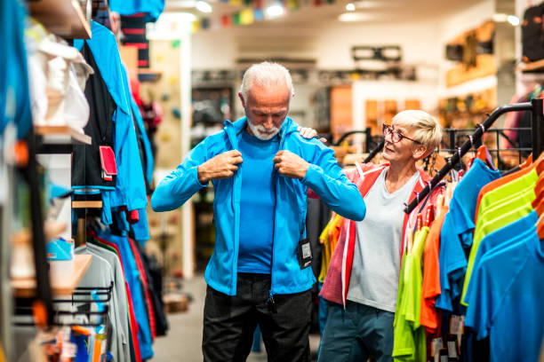 istock Elderly active man trying on a soft shell hiking jacket while his partner is watching in an outdoor equipment store 1241475925