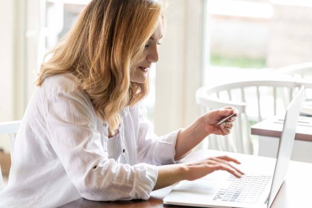 istock Young woman holding credit card and using laptop computer in cafe 1241480429