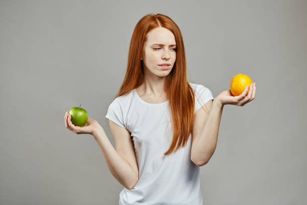 istock difficult choice. sceptical girl holding an apple and an orange 1241486156