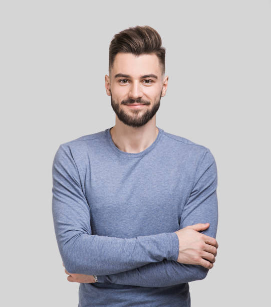 Portrait of handsome smiling young man with crossed arms Cheerful young man with crossed hands looking to the camera. Isolated on gray background one young man only stock pictures, royalty-free photos & images