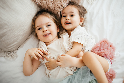 Cute sisters playing together in parent's bed, little girl looking at camera