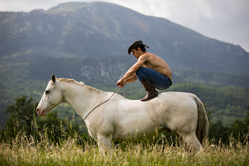 Young Adult Cowboy Crouching on Horse in Nature.