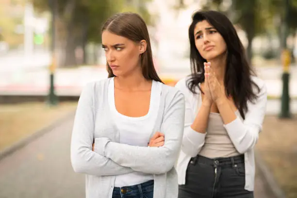 Photo of Girl Begging Offended Female Friend To Remain Friends Standing Outdoors