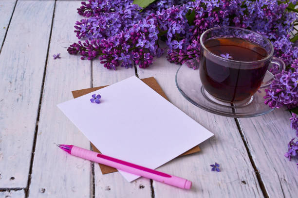 Cup of tea with lilac flowers on a wooden white background. Nearby lies a sheet of paper, and a pink pen. Mocap for postcards. Spring time. Vase with lilacs. Copy space for text. The concept of holidays and good morning wishes. taza de té con flores lilas sobre fondo blanco de madera. cerca se encuentra una hoja de papel, y un bolígrafo rosa. mocap para postales. hora de primavera. jarrón con lilas. copiar espacio para texto. el concepto de vacaciones y buenos deseos de la ma�