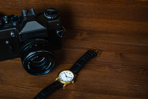 Retro photo camera and vintage golden wristwatch on a wood background.