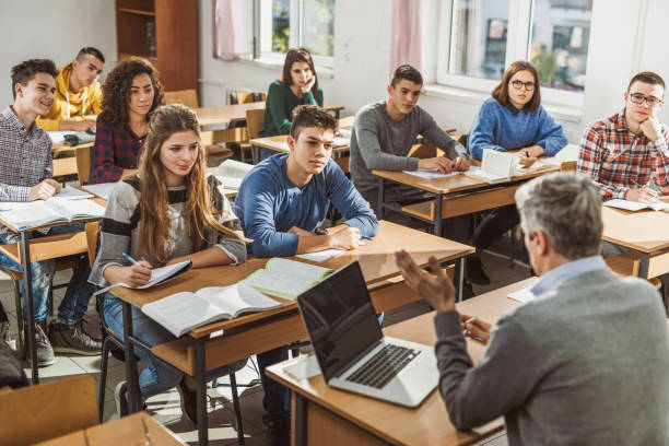 High school students listening to their teacher on a class. Large group of students listening to their teacher during a class at high school. high school building stock pictures, royalty-free photos & images
