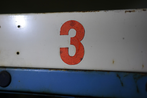 Old vintage hand painted red colored number 3  on white blue tin metal background