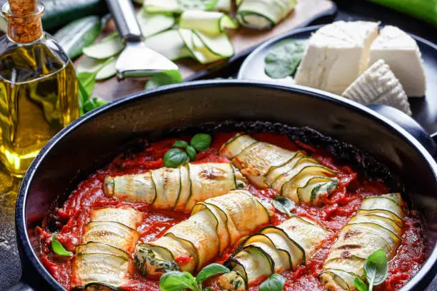 Zucchini lasagna rolls stuffed with ricotta mix of fresh baby spinach,  basil baked in tomato sauce served on a round black baking dish, fresh ricotta, olive oil, zucchini strips, close-up