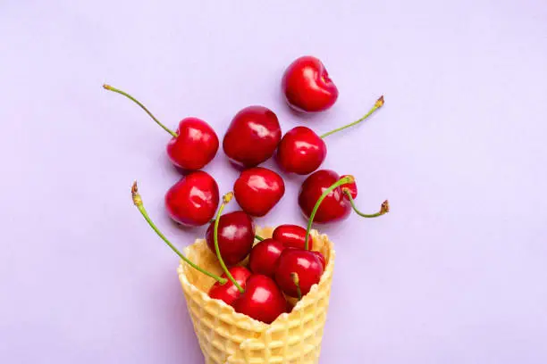 Fresh cherries in waffle cones Ice cream cone filled with fresh sweet cherry on lilac background. Top view. Copy space. Summer creative concept Flat lay Healthy food.