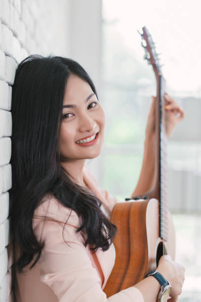 jovem mulher tocando guitarra na sala de estar, desfrutando de tempo despreocupado em casa. - 16721 - fotografias e filmes do acervo