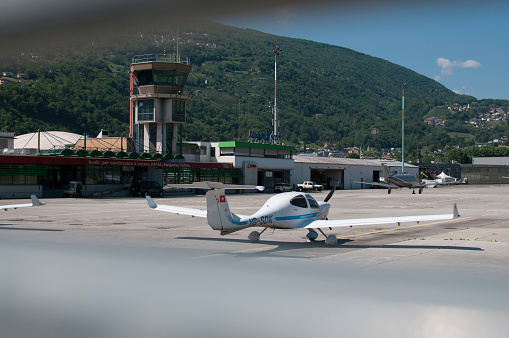 Agno, Ticino, Switzerland - 21st May 2020 : View through the gate of the Lugano-Agno airport in Switzerland with a small airplane parked in front of it