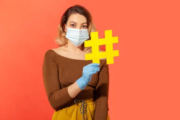 Photo of Stay home tagged message. Woman wearing surgical face mask gloves and holding hashtag symbol