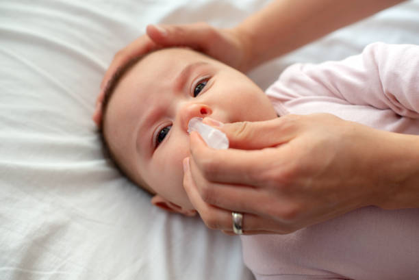 Close up of caring  mother with nasal pump to clean her baby's nose. Baby lying in bed stock photo