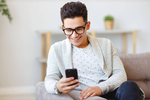 istock Cheerful ethnic male using smartphone on couch 1241648533