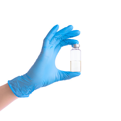 Medical theme: doctor's hand in a blue glove holding a vial of transparent liquid for injection. The scientist's hand holds a vial with vaccine isolated on white.