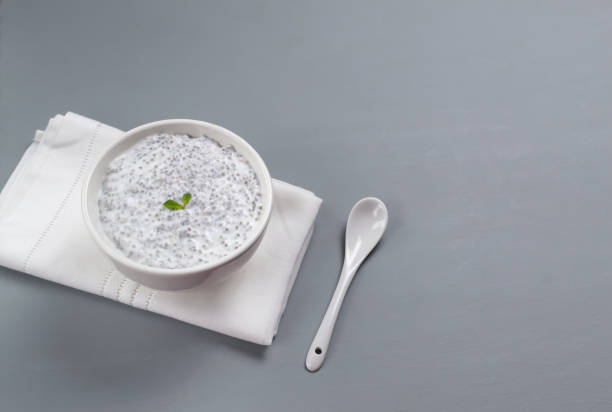 istock Chia pudding with small mint leaves in a white bowl and a teaspoon on a white napkin on a gray background. Copy space. 1241667697