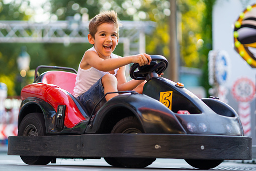 happy smiling 5 years old boy driving with go cart outdoors in summer, shallow focus background blurred