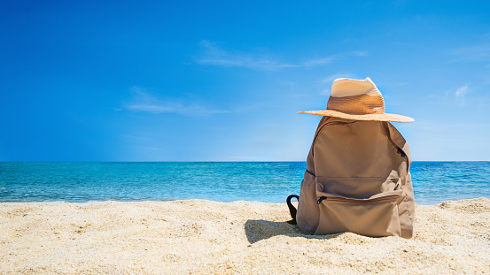 Beach straw hat and backpack  on the sea ocean beach backdrop. Space for text. Vacation and tourism concept. Sunstroke protective accessory