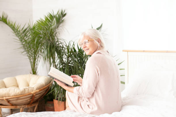 istock Senior woman sitting on bed with book. 1241688778
