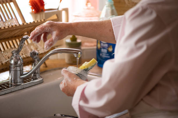 Soapy Hand Reaching to Turn Off Running Water in Kitchen Sink
