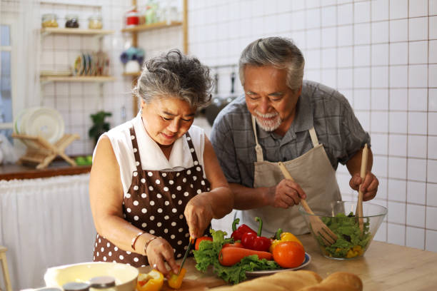 Happiness senior elderly couple having fun in kitchen with healthy food for working from home. COVID-19 stock photo