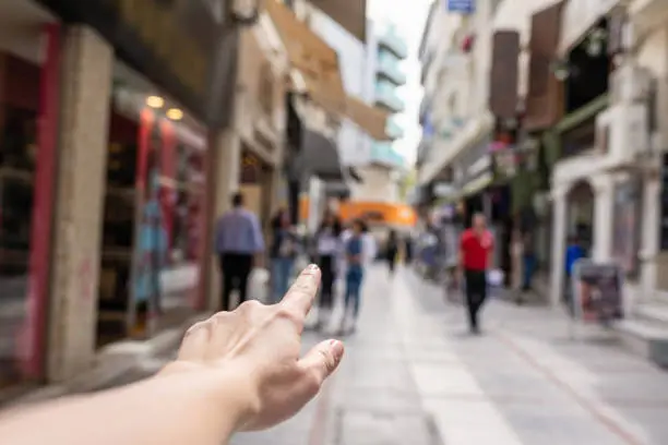 Photo of Girl shows finger on a shop of busy tourist street. Selective focus