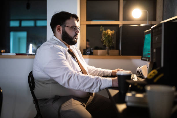 istock Overweight police detective using computer late at nigh at office 1241793600
