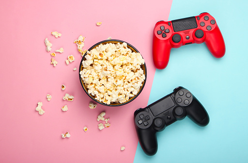 Two gamepads and a bowl of popcorn on pink blue pastel background. Gaming, leisure and entertainment concept. Top view