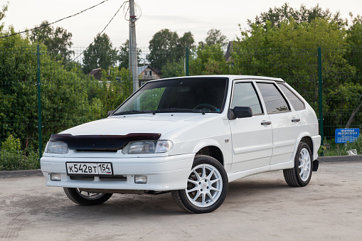 Novosibirsk, Russia - 05.20.2020: The new domestic Russian car brand Lada automobile industry VAZ model 2114 of a modern series of white color and drives against the background of green trees, a fence