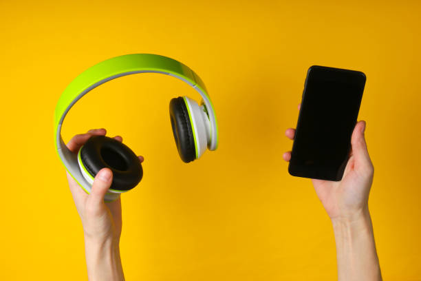 istock Hands hold stereo headphones and smartphone on a yellow background. Gadget sync 1241846372
