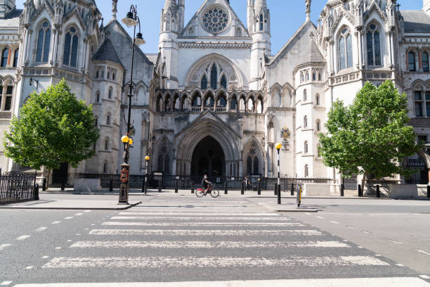 Closed Royal Courts of Justice in London due to Coronavirus COVID-19 with a cyclist in front wearing a face mask The Royal Courts of Justice are the most famous Courts in England and Wales are are often the site of famous cases.  This building regularly appears in the press and news coverage.  The image shows a lone cyclist wearing a face mask during the COVID-19 pandemic. royal courts of justice stock pictures, royalty-free photos & images