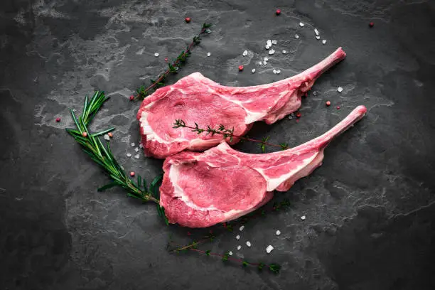 prepared for cooking raw steak of veal on the bone on the dark stone with rosemary and thyme