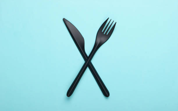 istock Black plastic knife with a fork on a blue background. Top view. Minimalism 1241849801