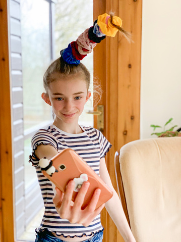 Young girl smiling taking a selfie at home. She has styled her hair with multiple scrunchies on top of her head.