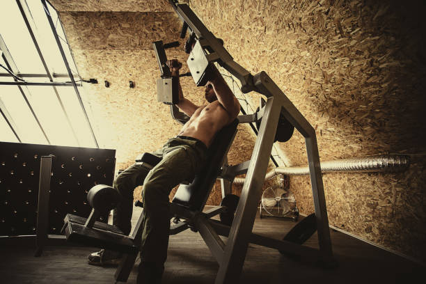 entrenamiento de hombre sin camisa en la máquina de ejercicios en el gimnasio - weight training weight bench weightlifting men fotografías e imágenes de stock