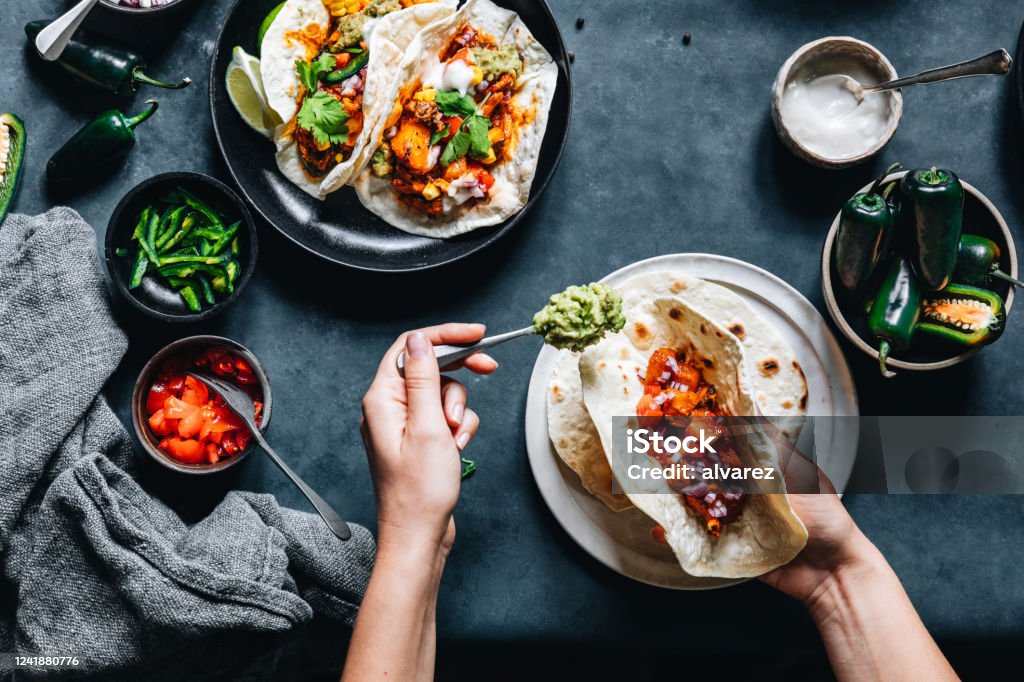 Woman preparing tasty vegan tacos Point of view shot of a woman preparing tasty vegan tacos in kitchen. Female hands put fillings in tacos. Taco Stock Photo