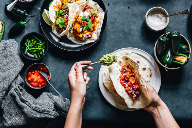 Woman preparing tasty vegan tacos Point of view shot of a woman preparing tasty vegan tacos in kitchen. Female hands put fillings in tacos. mexican food stock pictures, royalty-free photos & images
