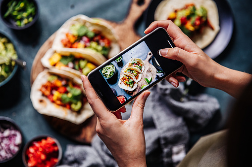 Hand of a chef taking photograph of tacos on table with a mobile phone. Hands of cook photographing Mexican food .