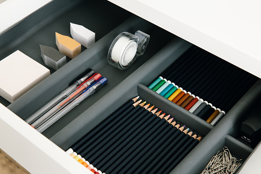 Office supplies in desktop drawer. Writing pens, pencils, paper clips, color sheets for notes. Workplace order. Work at home.
