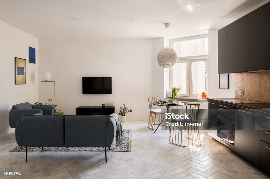 Living room, dining table and kitchen Apartment with simple living room, elegant dining table with stylish chairs and modern black kitchen in one room Flooring Stock Photo