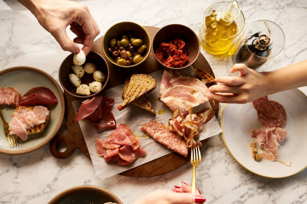 Traditional Spanish tapas for sharing with friends. Friends Sharing Italian Antipasti with Olives, Sundried Tomato Pesto, Pickled Vegetables, Bocconcini, Bresaola, Beef Pancetta, Smoked Beef, Veal Cotto, from above, appetizers on a table. Traditional Spanish tapas for sharing with friends. antipasto stock pictures, royalty-free photos & images