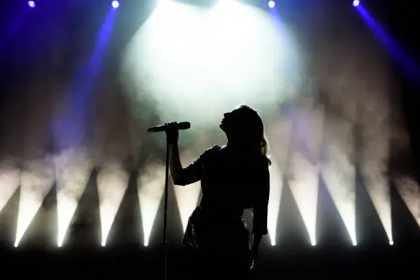 Photo of Silhouette of singer on stage. Dark background, smoke, spotlights.