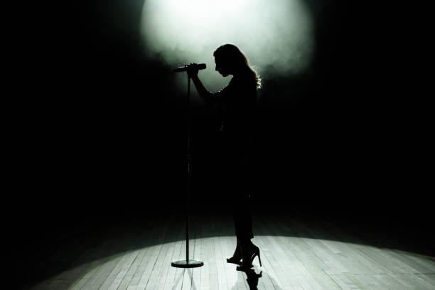 silhouette nera della cantante femminile con faretti bianchi sullo sfondo - microphone stage music popular music concert foto e immagini stock