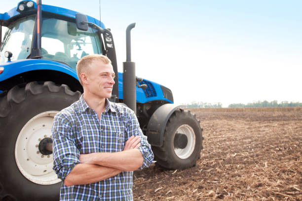 Joven atractivo cerca de un tractor. Conductor del tractor. Concepto de agricultura y obras de campo. - foto de stock