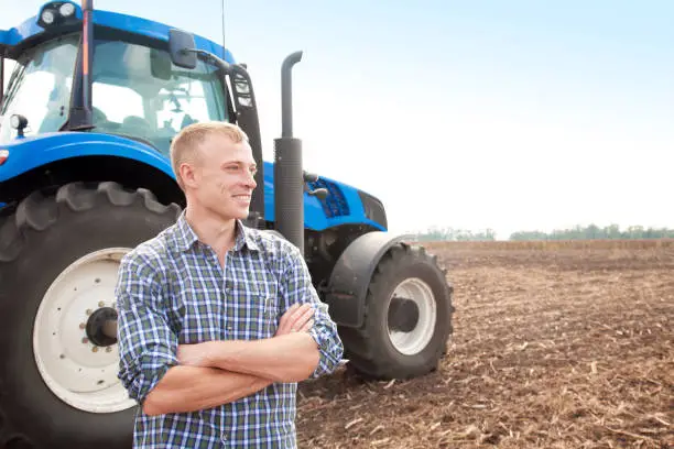 Young attractive man near a tractor. Tractor driver. Concept of agriculture and field works.