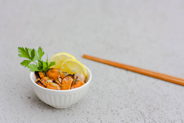 Mussels without shell with lemon slices in white ceramic bowl. Seafood concept. Selective focus. Space for text.