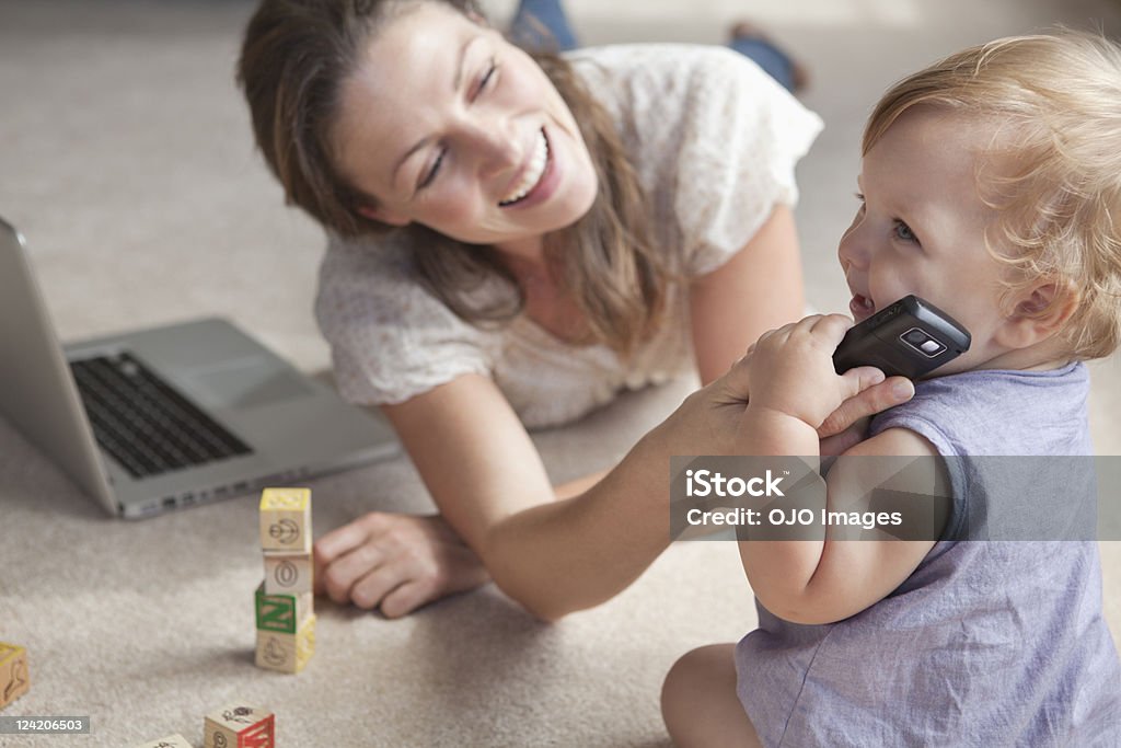 Donna sorridente che lavora su un computer portatile mentre bambino giocando - Foto stock royalty-free di 12-17 mesi